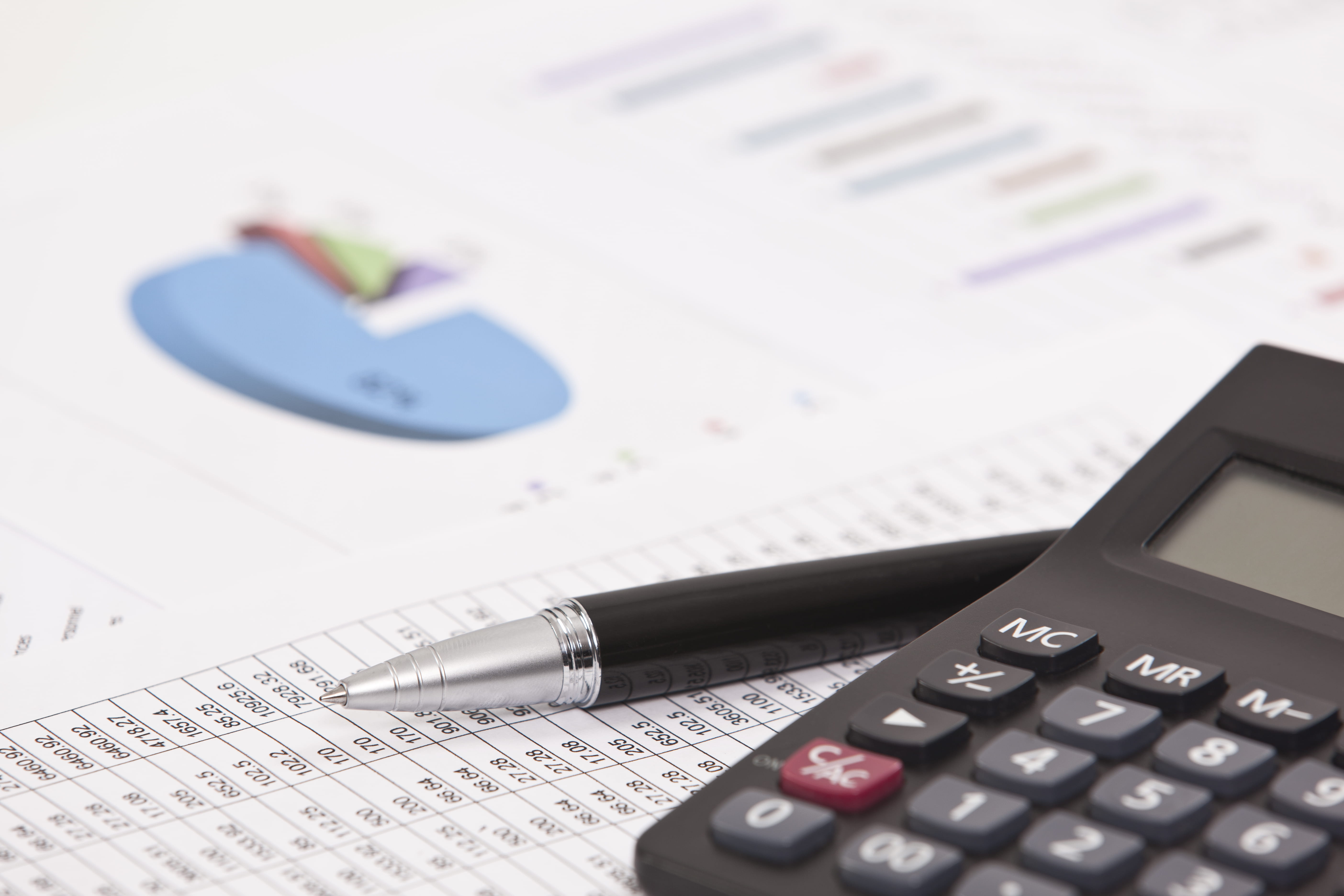 Calculator beside a pen and financial analysis paper